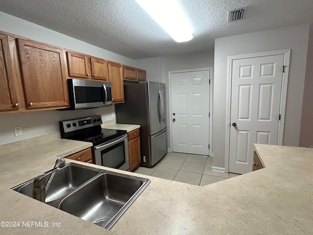 kitchen with appliances with stainless steel finishes, sink, light tile patterned floors, and a textured ceiling