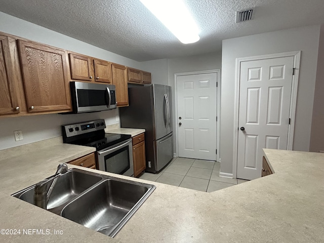 kitchen featuring appliances with stainless steel finishes, a sink, a textured ceiling, brown cabinets, and light countertops