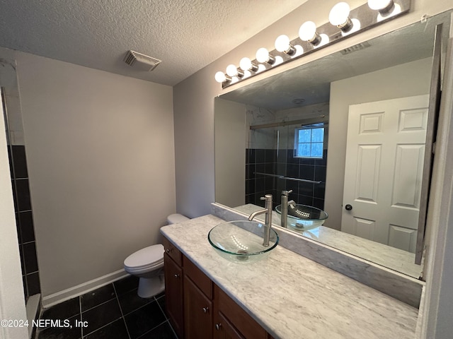 bathroom with tile patterned floors, a tile shower, toilet, vanity, and a textured ceiling
