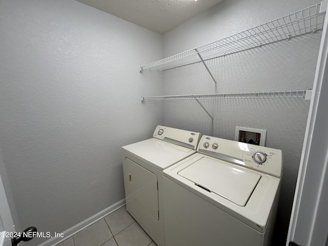 laundry area with washer and dryer, light tile patterned floors, a textured wall, and baseboards