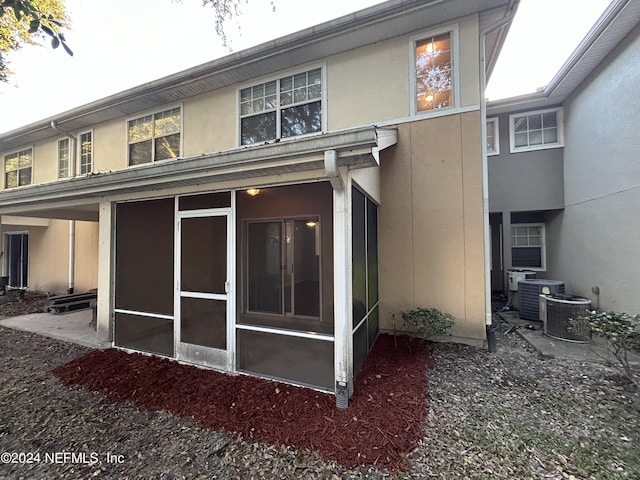 back of property with a sunroom, stucco siding, and central AC