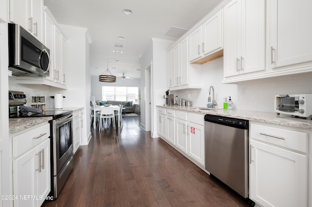 kitchen with light stone countertops, stainless steel appliances, dark wood-type flooring, white cabinetry, and backsplash