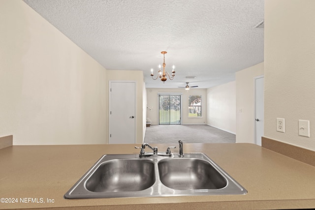 kitchen with pendant lighting, sink, ceiling fan with notable chandelier, and a textured ceiling