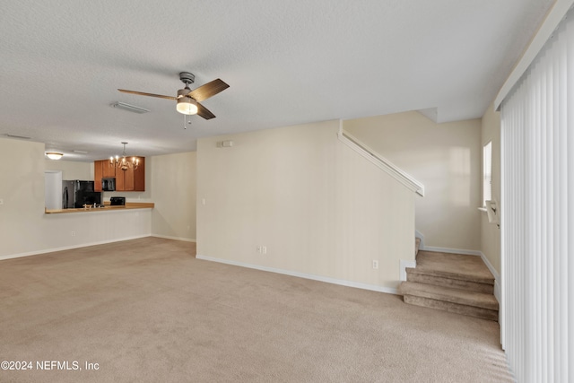 unfurnished living room with a textured ceiling, light colored carpet, and ceiling fan with notable chandelier