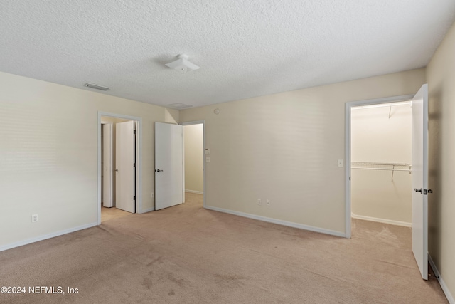 unfurnished bedroom with a textured ceiling, light carpet, a walk in closet, and a closet