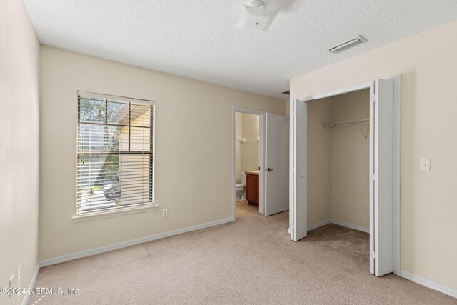 unfurnished bedroom featuring a textured ceiling, ensuite bathroom, light carpet, and a closet