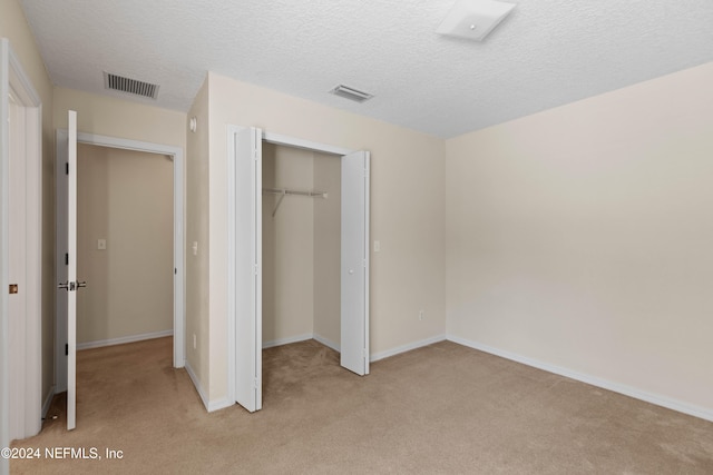 unfurnished bedroom with a closet, a textured ceiling, and light colored carpet