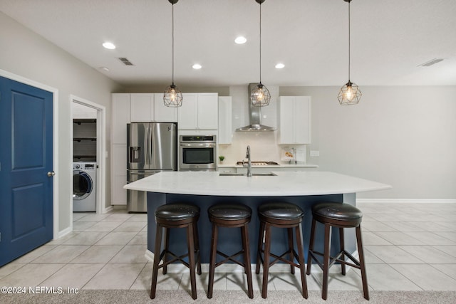 kitchen with appliances with stainless steel finishes, washer / clothes dryer, an island with sink, and white cabinets