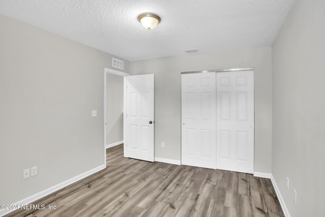 unfurnished bedroom with a textured ceiling, light hardwood / wood-style flooring, and a closet