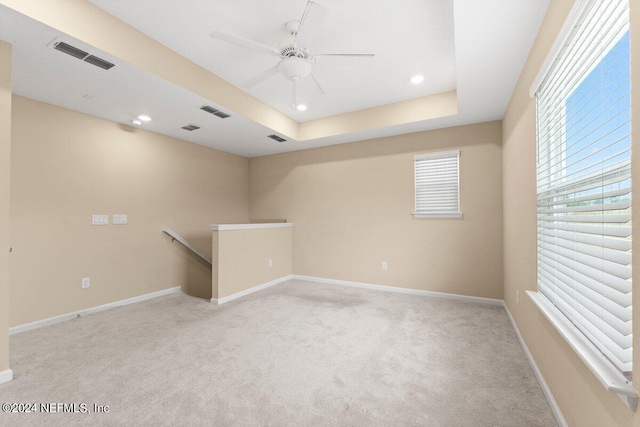 unfurnished room with ceiling fan, light carpet, and a tray ceiling