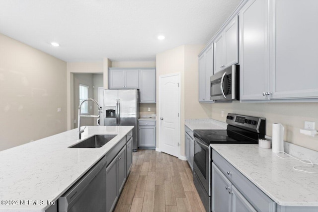 kitchen with light stone counters, sink, gray cabinets, appliances with stainless steel finishes, and light wood-type flooring