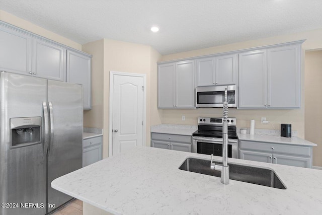 kitchen featuring light stone counters, gray cabinets, appliances with stainless steel finishes, and sink