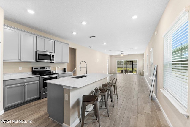 kitchen with gray cabinets, a kitchen island with sink, light hardwood / wood-style flooring, sink, and appliances with stainless steel finishes