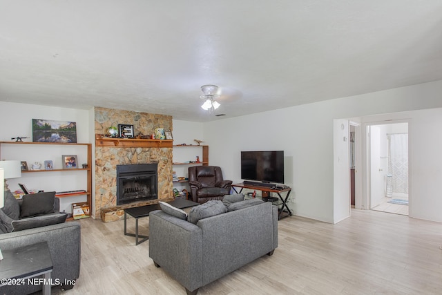 living room featuring ceiling fan, a stone fireplace, and light hardwood / wood-style flooring