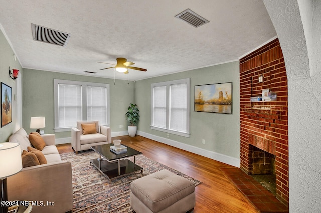 living room featuring ceiling fan, a fireplace, wood-type flooring, and a textured ceiling