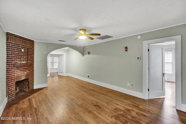 unfurnished living room with ceiling fan, a brick fireplace, a textured ceiling, hardwood / wood-style flooring, and ornamental molding