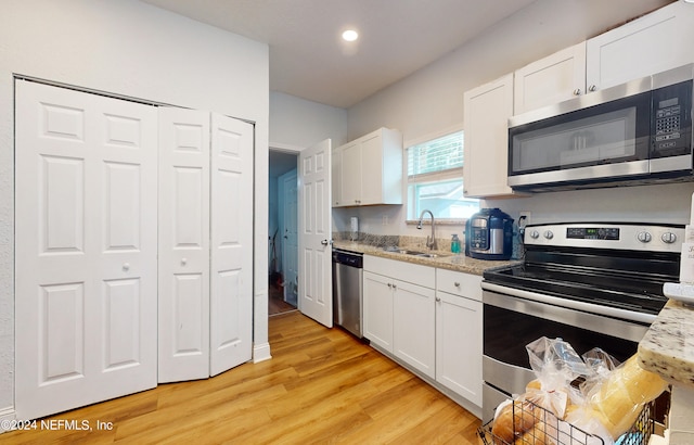 kitchen with light wood-type flooring, light stone countertops, stainless steel appliances, sink, and white cabinetry