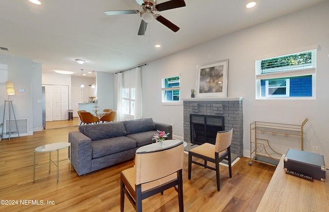 living room with a brick fireplace, light hardwood / wood-style flooring, and ceiling fan