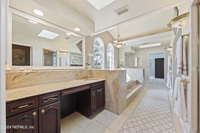 bathroom featuring a chandelier, a skylight, vanity, tiled tub, and tile patterned flooring