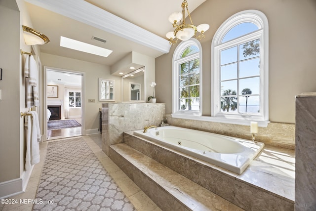 bathroom featuring an inviting chandelier, lofted ceiling with skylight, tile patterned flooring, and tiled bath