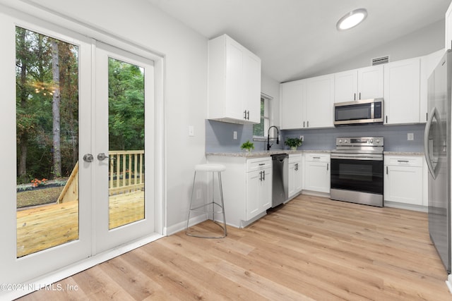 kitchen featuring light stone countertops, light hardwood / wood-style floors, white cabinetry, vaulted ceiling, and appliances with stainless steel finishes