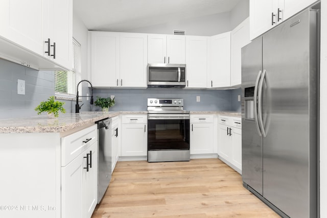 kitchen with lofted ceiling, light stone countertops, stainless steel appliances, white cabinetry, and light hardwood / wood-style flooring