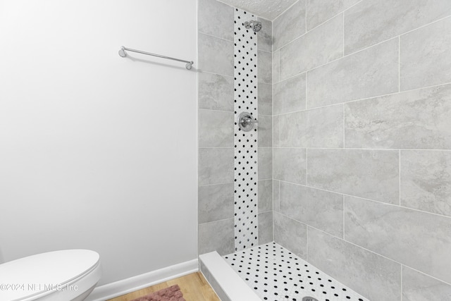 bathroom with hardwood / wood-style flooring, tiled shower, and toilet