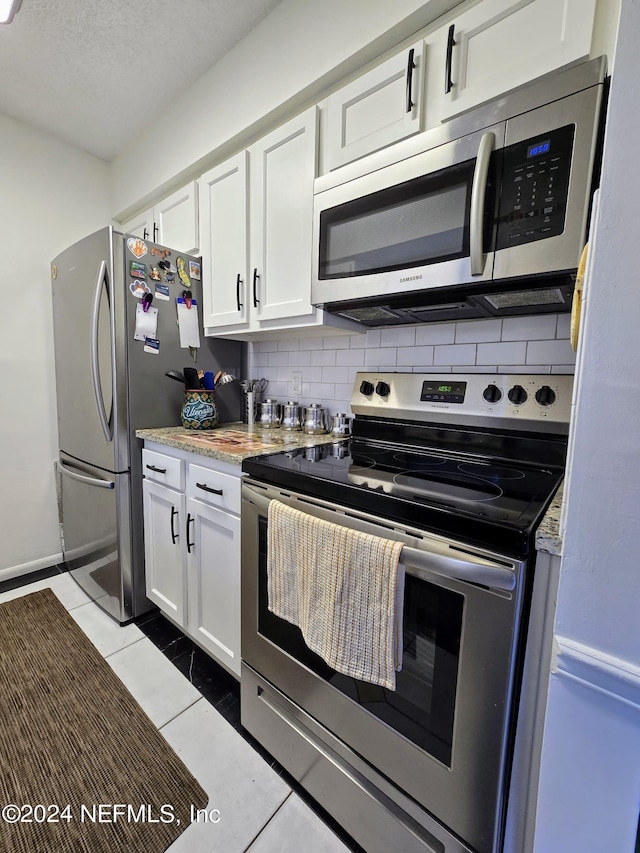 kitchen with light stone counters, decorative backsplash, stainless steel appliances, white cabinetry, and light tile patterned floors