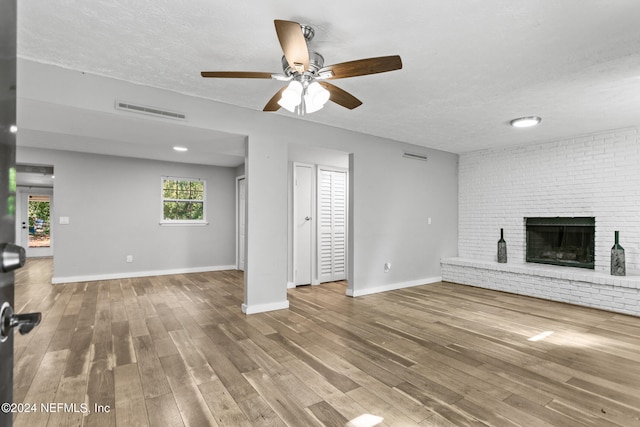 unfurnished living room with ceiling fan, wood-type flooring, a textured ceiling, and a fireplace