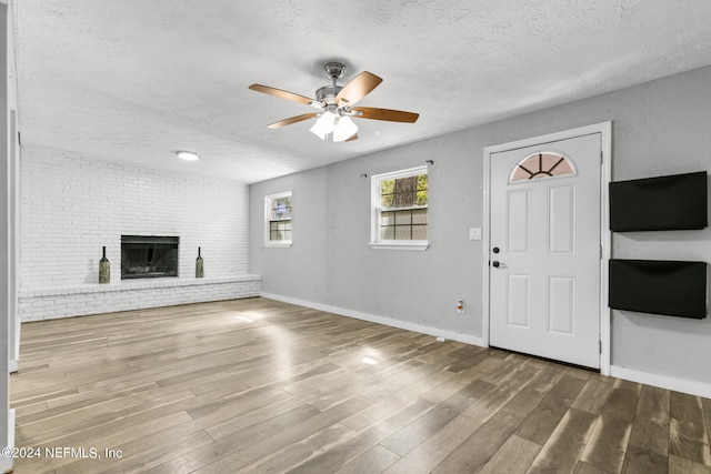 unfurnished living room with a textured ceiling, ceiling fan, wood-type flooring, and a brick fireplace