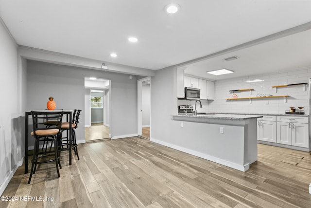 kitchen with light hardwood / wood-style flooring, tasteful backsplash, sink, white cabinetry, and a breakfast bar