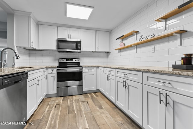 kitchen featuring stainless steel appliances, backsplash, sink, light wood-type flooring, and white cabinetry