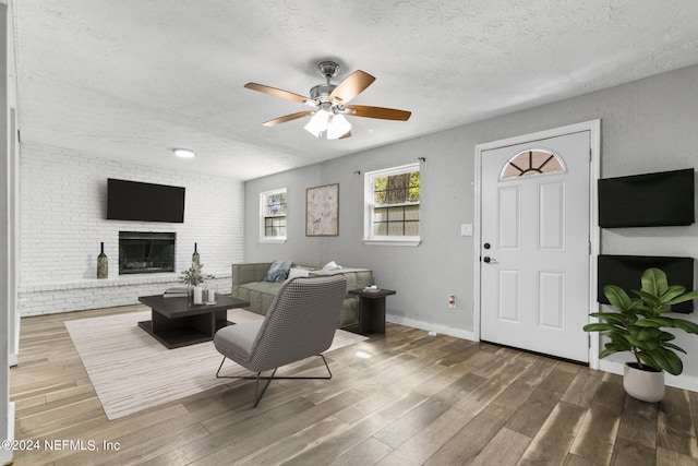 living room featuring hardwood / wood-style floors, a brick fireplace, a textured ceiling, and ceiling fan