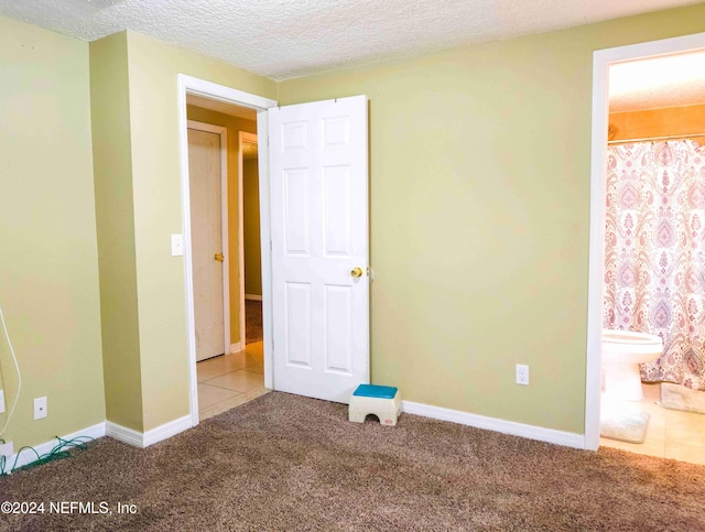 unfurnished bedroom featuring carpet floors, ensuite bathroom, and a textured ceiling