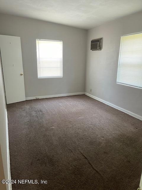 empty room with dark colored carpet and a wall unit AC