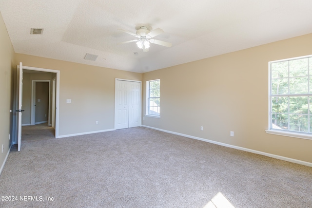 unfurnished bedroom featuring light carpet, a textured ceiling, a closet, and ceiling fan