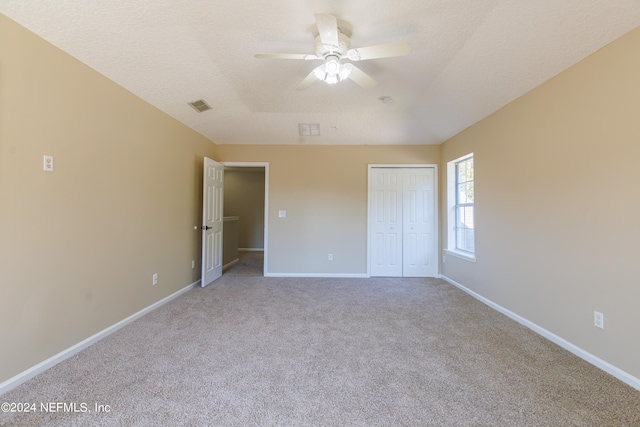 unfurnished bedroom with light carpet, a textured ceiling, a closet, and ceiling fan