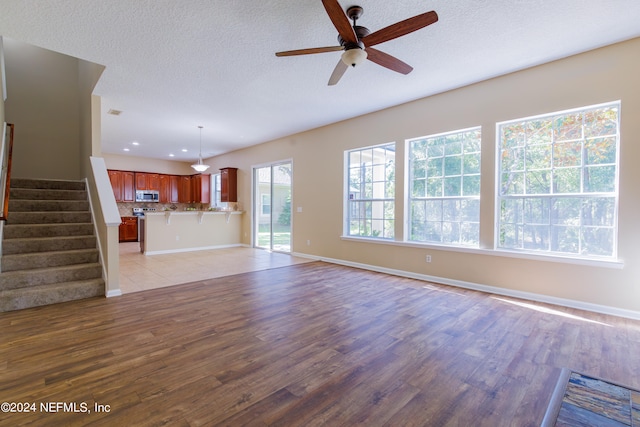 unfurnished living room featuring light hardwood / wood-style flooring, a textured ceiling, and ceiling fan