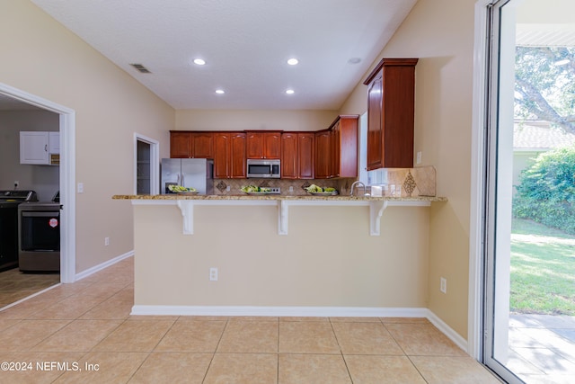 kitchen featuring stainless steel appliances, decorative backsplash, a wealth of natural light, and a kitchen breakfast bar