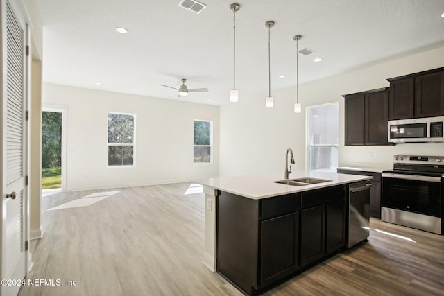 kitchen featuring sink, stainless steel appliances, decorative light fixtures, light hardwood / wood-style flooring, and a kitchen island with sink