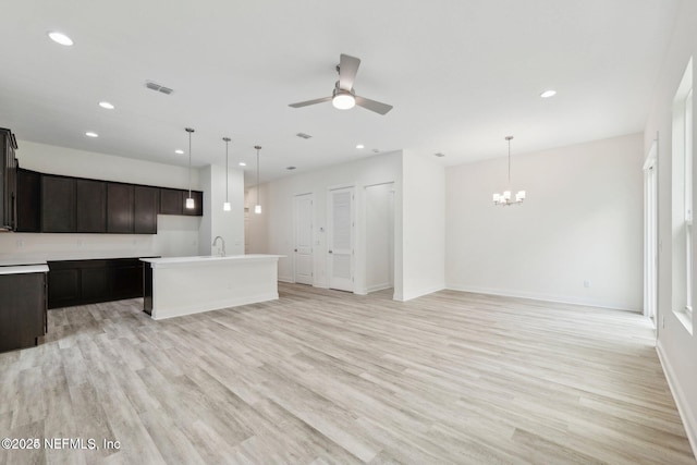 kitchen featuring ceiling fan with notable chandelier, hanging light fixtures, a center island with sink, and light hardwood / wood-style flooring