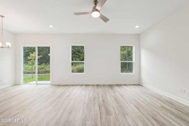 unfurnished room featuring plenty of natural light, ceiling fan with notable chandelier, and light hardwood / wood-style floors