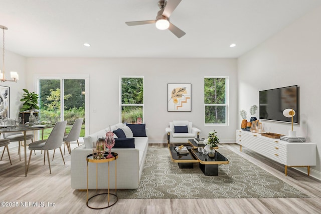 living room featuring ceiling fan with notable chandelier, wood-type flooring, and a healthy amount of sunlight