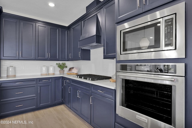 kitchen featuring custom exhaust hood, blue cabinetry, appliances with stainless steel finishes, and a textured ceiling