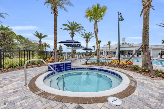 community pool with a patio area, fence, and a hot tub