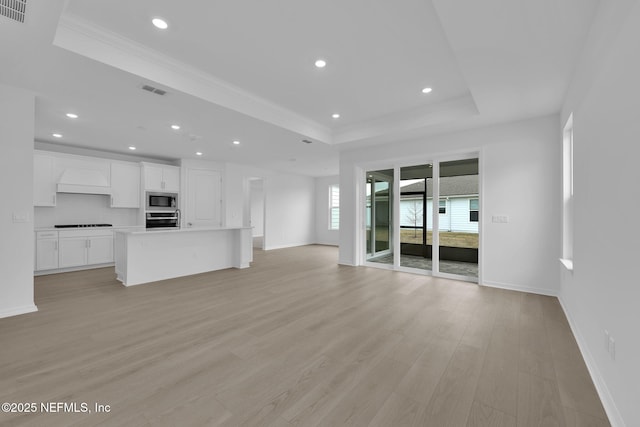 unfurnished living room with recessed lighting, light wood-style flooring, a tray ceiling, and ornamental molding