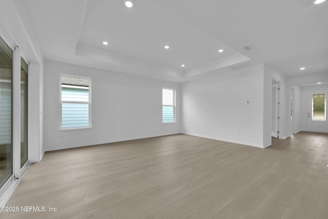 empty room featuring light wood-type flooring, a raised ceiling, baseboards, and visible vents