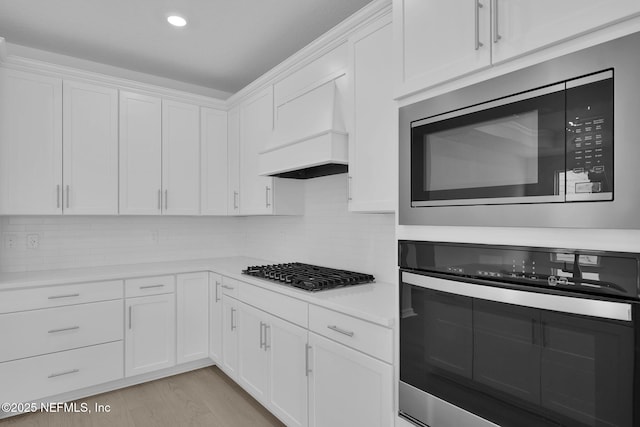 kitchen with backsplash, appliances with stainless steel finishes, white cabinets, light countertops, and custom exhaust hood