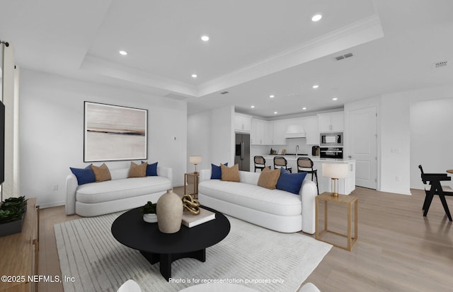 living area featuring visible vents, a raised ceiling, light wood-style flooring, and crown molding