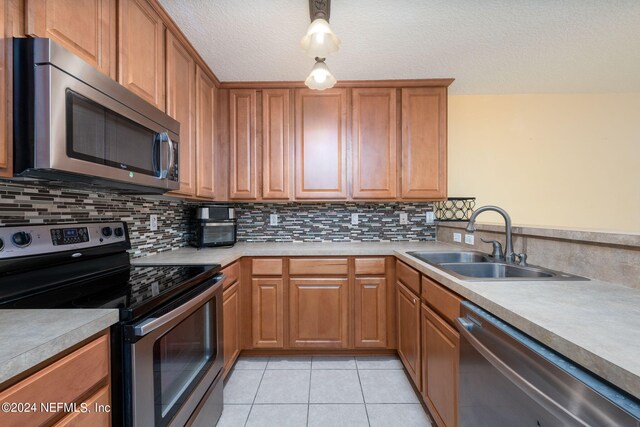 kitchen with decorative backsplash, appliances with stainless steel finishes, a textured ceiling, light tile patterned flooring, and sink